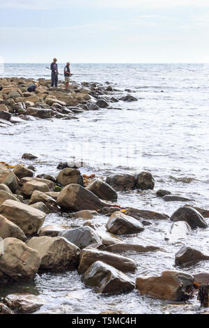 Un homme et deux garçons à la pêche dans la mer sur un promontoire rocheux à Kimmeridge Bay, Dorset, England, UK Banque D'Images