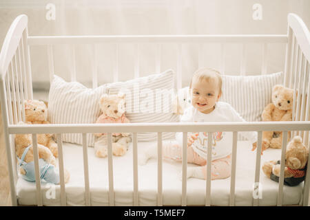 L'enfant est assis dans un lit et joue parmi les oreillers et les ours en peluche. Banque D'Images