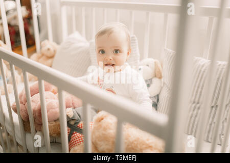 L'enfant est assis dans un lit et joue parmi les oreillers et les ours en peluche. Banque D'Images