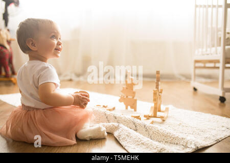 Bébé fille s'assied sur le tapis et joue dans la pépinière. Banque D'Images