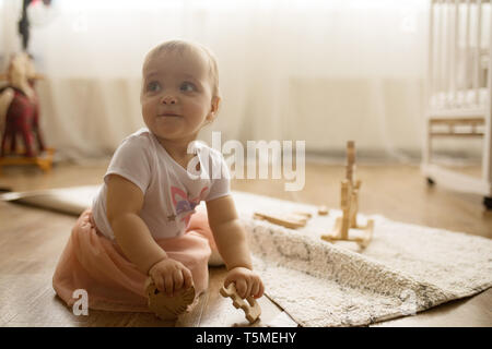 Bébé fille s'assied sur le tapis et joue dans la pépinière. Banque D'Images