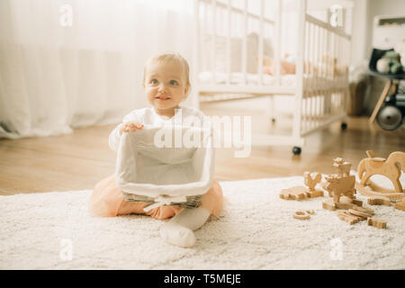 Bébé fille s'assied sur le tapis parmi les jouets en bois et joue avec panier dans la pépinière. Banque D'Images