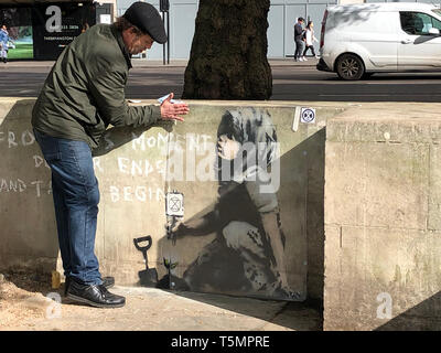 Calvin Benson, 48, met une feuille de plastique de protection sur une oeuvre qui semble être l'artiste de rue par Banksy. L'artwork est apparue près de l'extinction dans le camp de la rébellion, London. Banque D'Images