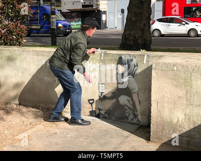 Calvin Benson, 48, met une feuille de plastique de protection sur une oeuvre qui semble être l'artiste de rue par Banksy. L'artwork est apparue près de l'extinction dans le camp de la rébellion, London. Banque D'Images