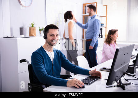 Mobilité homme assis sur fauteuil roulant working on Computer in Office Banque D'Images