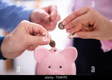 La main d'affaires Introduction de pièces en rose Tirelire In Office Banque D'Images
