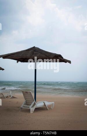 Tempête sur la mer avec des nuages orageux. Parasol et transats inversée sous parasol sur la plage Banque D'Images