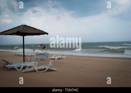 Tempête sur la mer avec des nuages orageux. Parasol et transats inversée sous parasol sur la plage Banque D'Images