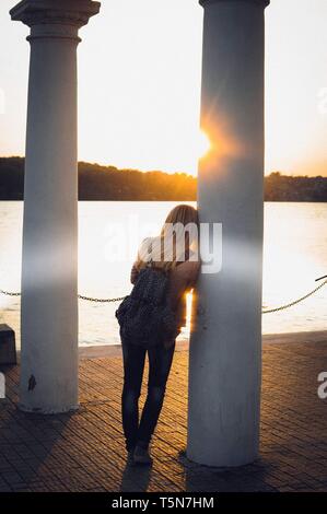 Fille avec sac à dos à la recherche sur le coucher du soleil près du pilier et du lac Banque D'Images