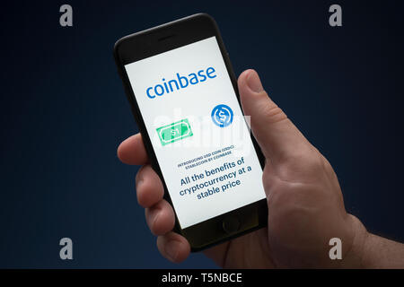 Un homme se penche sur son iPhone qui affiche le logo Coinbase (usage éditorial uniquement). Banque D'Images