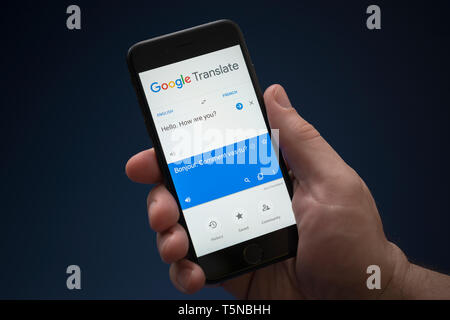 Un homme se penche sur son iPhone qui affiche le logo Google Translate (usage éditorial uniquement). Banque D'Images