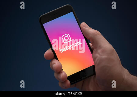 Un homme se penche sur son iPhone qui affiche le logo d'Instagram (usage éditorial uniquement). Banque D'Images