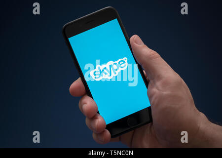 Un homme se penche sur son iPhone qui affiche le logo Skype (usage éditorial uniquement). Banque D'Images