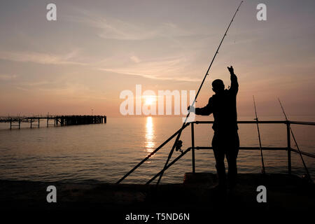 La pêche à la ligne d'accouplement à l'aide de pêcheurs beach dominante de la passerelle au-dessus de Totland Bay alors que le soleil se couche sur l'horizon lointain et Totland Pier. Banque D'Images
