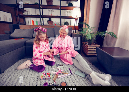 Granny et girl à peignoirs assis sur marbre et en choisissant les épingles Banque D'Images