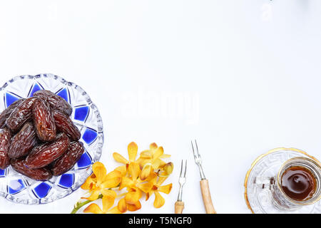 Ramadan concept montrant beaucoup de dattiers dans un modèle islamique bol avec un verre de thé et fleurs orchidée jaune sur un fond blanc Banque D'Images