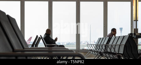 La borne 4,l'aéroport de Heathrow, Londres, Royaume-Uni 22 avril 2019. Deux hommes à l'aide de téléphones intelligents sont assis à une porte dans l'attente de l'aéroport à bord d'un vol Banque D'Images