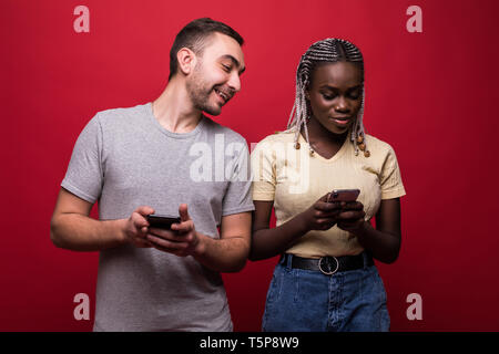 Portrait de race mixte homme et femme froncer et regarder chaque autres des téléphones cellulaires sur fond rouge Banque D'Images