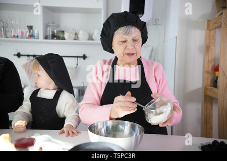 Famille faire des crêpes. Une vieille femme de mettre la pâte sur le moule Banque D'Images