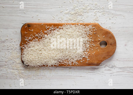 Basmati riz blanc sec sur une planche en bois rustique blanc sur fond de bois, vue du dessus. Les frais généraux, de dessus, de mise à plat. Banque D'Images