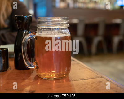 Pot Mason mug avec poignée rempli de bière à côté de bouteille de sake au restaurant Banque D'Images