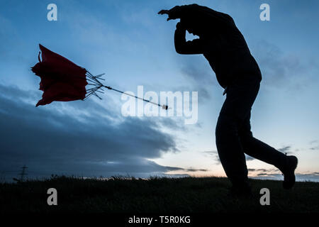 Homme avec un parapluie rouge le jour du vent/de l'orage. ROYAUME-UNI Banque D'Images