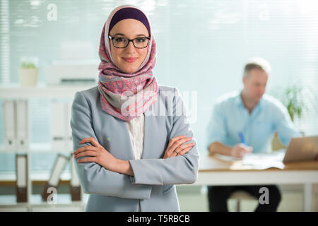 Belle jeune femme qui travaille à l'hijab, costume et lunettes standing in office, en souriant. Portrait of businesswoman musulmane. Wit bureau moderne Banque D'Images