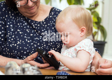 Heureux grand-mère et petite-fille mignon en utilisant smartphone, salon de l'enseignement Banque D'Images