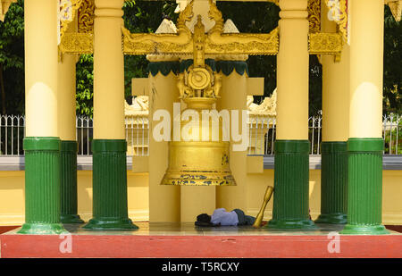 Un homme est en train de dormir sous un couvert d'or (Bonsho bell bouddhiste) dans un temple bouddhiste au cours d'une chaude journée ensoleillée. Bagan, Myanmar. Banque D'Images