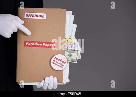 L'homme en costume et gants blancs tenir dossier papier avec Paradise Papiers et étiquette Offshore avec des documents et de l'argent à l'intérieur, fiscalité attrayante fuite documents conc Banque D'Images