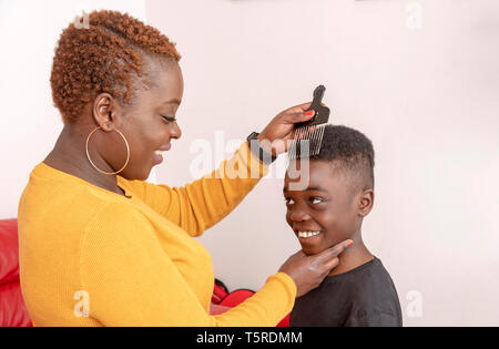 Andover, Hampshire, England, UK. Avril 2019. Un garçon de neuf ans avec des cheveux bouclés avec sa mère à l'aide d'un peigne afro à dents larges pour ses cheveux. Banque D'Images