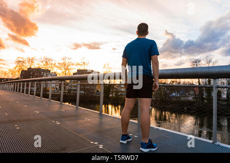 Vue arrière homme sportif relaxant après une longue course en regardant le coucher du soleil sur la ville. Activités récréatives.Self concept concept surmonter les obstacles, la conquête Banque D'Images