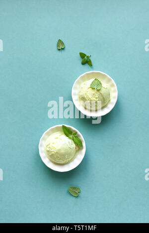 La crème glacée verte sur fond bleu, vue de dessus, copiez l'espace. Pistache vert, l'avocat ou le thé vert gelato dans cups avec feuille de menthe. Banque D'Images