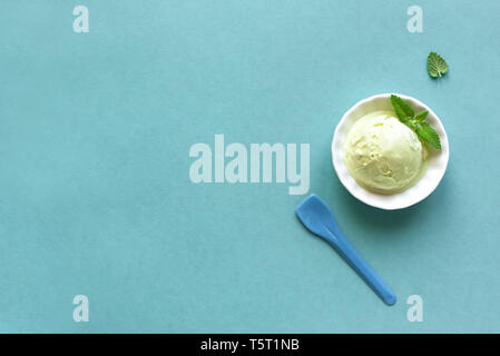 La crème glacée verte sur fond bleu, vue de dessus, copiez l'espace. Pistache vert, l'avocat ou le thé vert gelato en tasse avec feuille de menthe. Banque D'Images