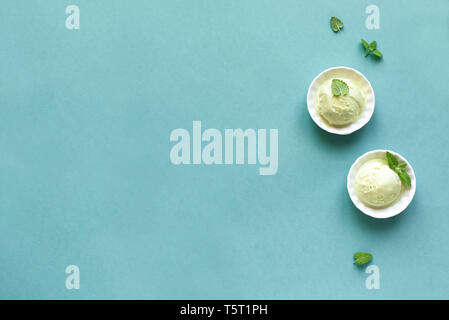 La crème glacée verte sur fond bleu, vue de dessus, copiez l'espace. Pistache vert, l'avocat ou le thé vert gelato dans cups avec feuille de menthe. Banque D'Images