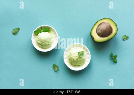 La crème glacée d'avocat sur fond bleu, vue de dessus, copiez l'espace. Vegan vert pistache ou avocat gelato ice cream avec les feuilles de menthe. Banque D'Images