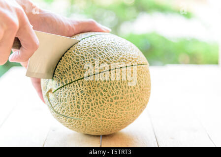 L'utilisation de l'homme divisé le couteau sur la plaque de bois melon orange Banque D'Images