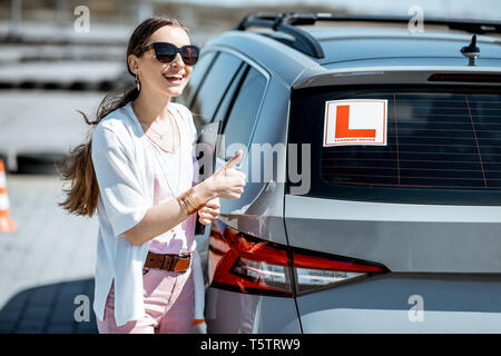 Portrait d'une jeune étudiante, debout près de la voiture d'apprentissage sur le terrain d'entraînement à l'école des pilotes Banque D'Images