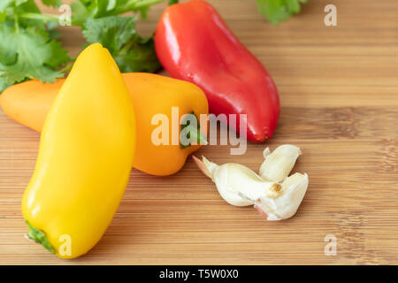 Planche à découper avec du jaune, rouge et orange bell mini poivrons, d'ail et persil Banque D'Images