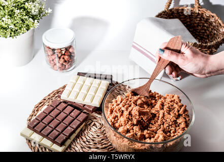 Une femme faisant 3 chocolats Tarte gâteau, les ingrédients sur la table. Cuisine équipée, sombre et de chocolat au lait. Les noisettes jar. La pâte à biscuits Banque D'Images