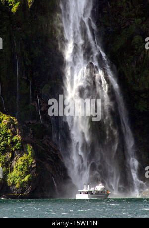 Milford Sound, Nouvelle Zélande- belle dame Bowen Falls avec un bateau sur le point de passer derrière eux. Banque D'Images