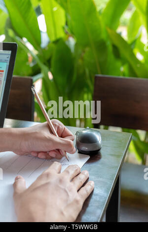 L'homme asiatique a écrit le budget avec un crayon dans la main gauche, côté à l'étude, à l'outdoor et feuille verte derrière. Banque D'Images