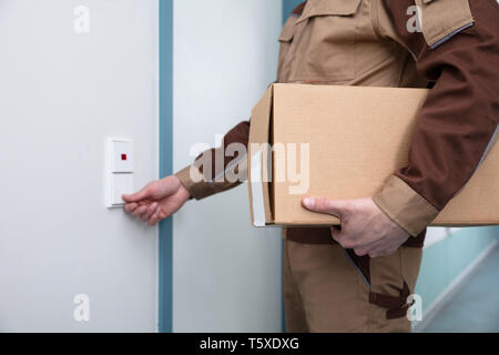 La mi-section de Delivery Man Holding Cardboard Box Faire sonner la cloche de porte Banque D'Images