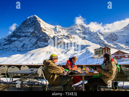 Les gens assis à l'extérieur restaurant / bar, avec face nord de l'Eiger derrière, en hiver. Kleine Scheidegg, Oberland Bernois, Suisse (Suisse) Banque D'Images