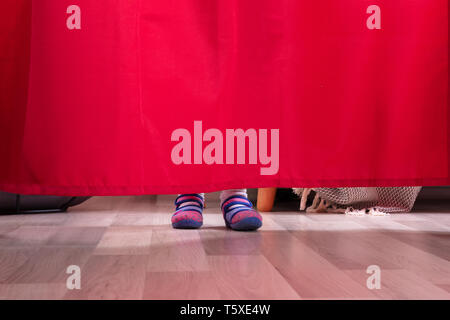 La section basse d'un Girl's pieds derrière le rideau sur plancher de bois franc Banque D'Images