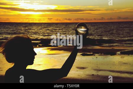 Silhouette de femme tenant une boule de cristal en beau coucher de soleil sur Ko Lanta, Thaïlande Banque D'Images