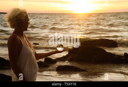 Femme blonde dans le soleil du soir tenant une boule de cristal sur Ko Lanta, Thaïlande Banque D'Images