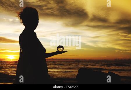 Silhouette of woman holding crystal ball contre l'horizon dans le soleil du soir sur Ko Lanta, Thaïlande Banque D'Images