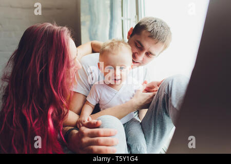 Famille heureuse de la mère, le père et fils de l'enfant de jouer et de câlins à la maison sur le sol près d'une grande fenêtre. Banque D'Images