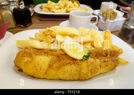 Un traditionnel fish and chips anglais repas servi sur une table dans un restaurant fish and chips. Les plaques contient des plaquettes et battues, morue plateau Banque D'Images